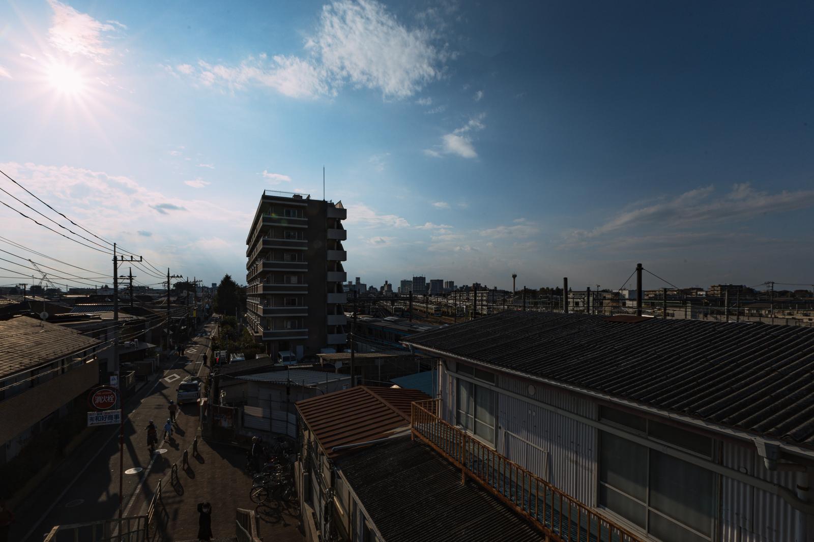 三鷹跨線橋から見た町並みと線路、手前にアパート、奥に建物群が見える昼間の景観