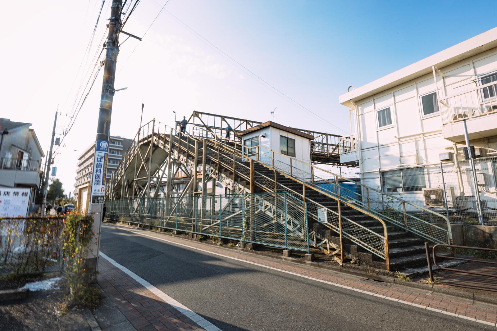 三鷹のJR線を跨ぐ金属製の陸橋と階段。周囲に住宅が立ち並ぶ