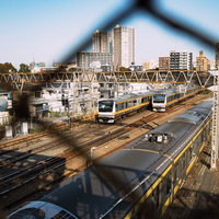 三鷹の陸橋から金網越しに見る中央線と駅周辺の町並みの写真