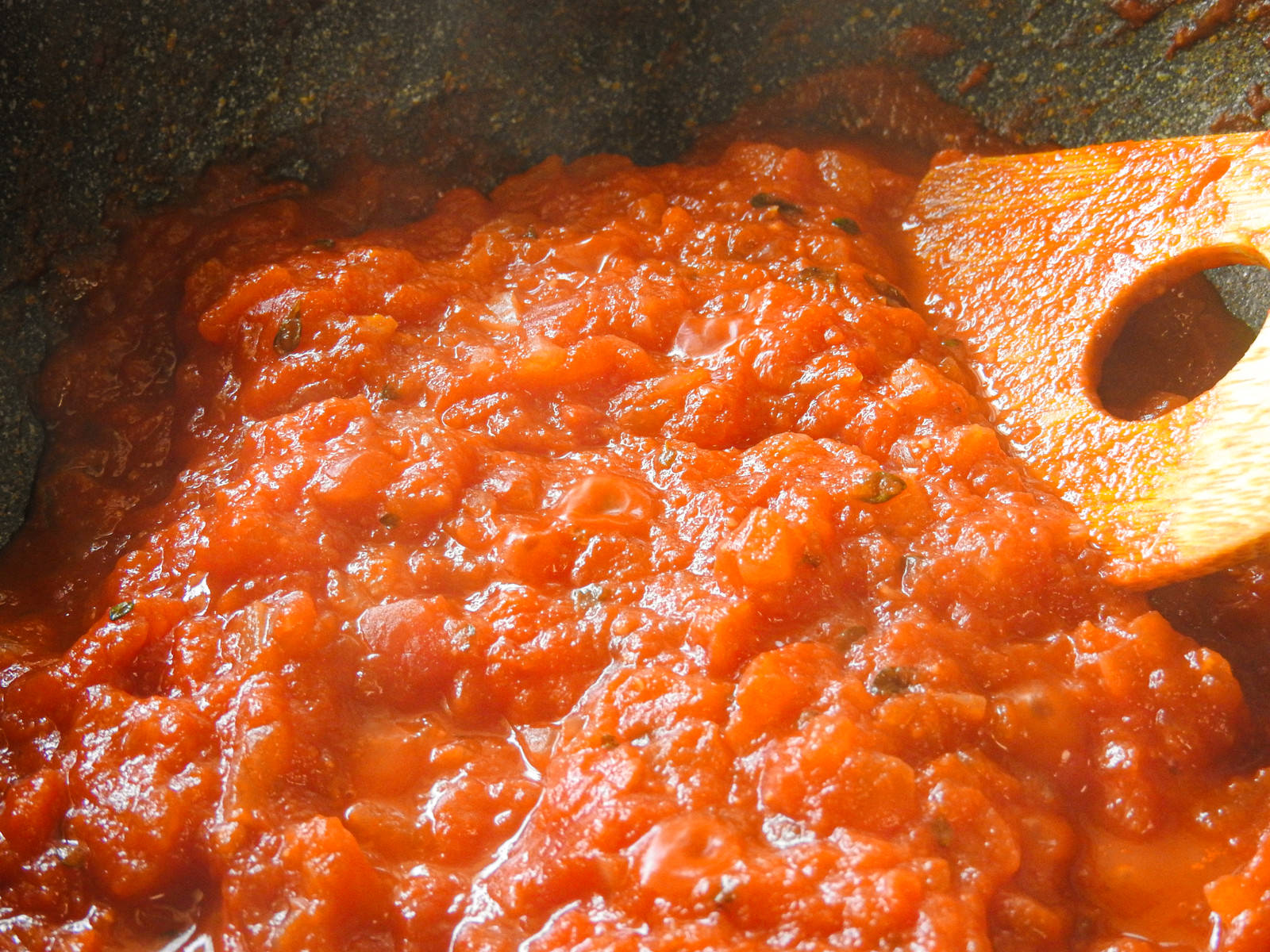 Red tomato sauce simmering in a frying pan with a wooden spoon