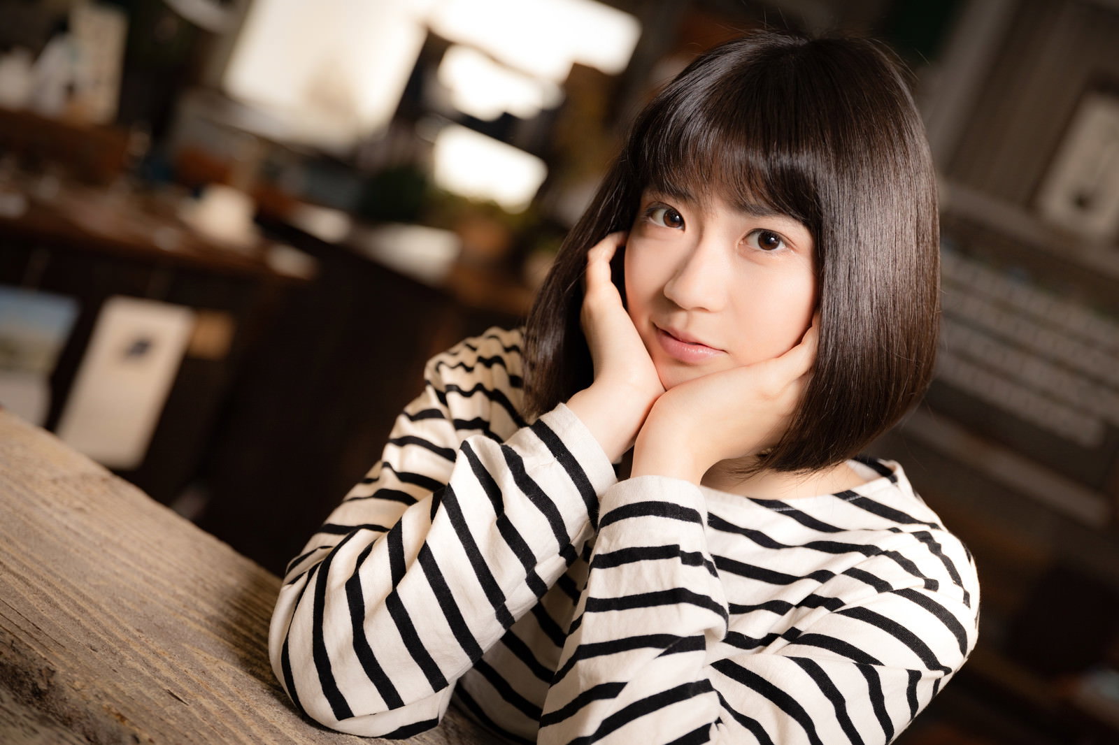 カフェのテーブルで頬杖をついて座るボーダーシャツの女性［モデル：塩田みう］
