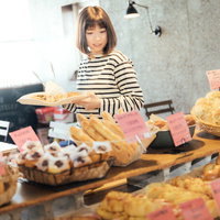 手作りパンのお店でトレイを手に取り焼きたてパンを選ぶ女性の写真