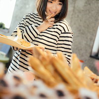 お腹が空いたからもうひとつ食べちゃおう、ボーダーシャツの女性がパン屋で菓子パンを選ぶの写真