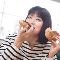 ボーダーシャツの女性が手作りパンを両手に頬張るの写真