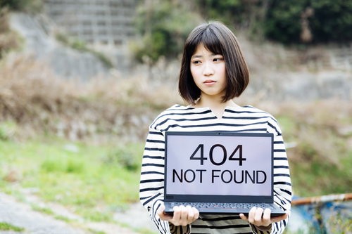 404エラーメッセージを表示するパソコンを持ち、ページが見つからず困惑する女性