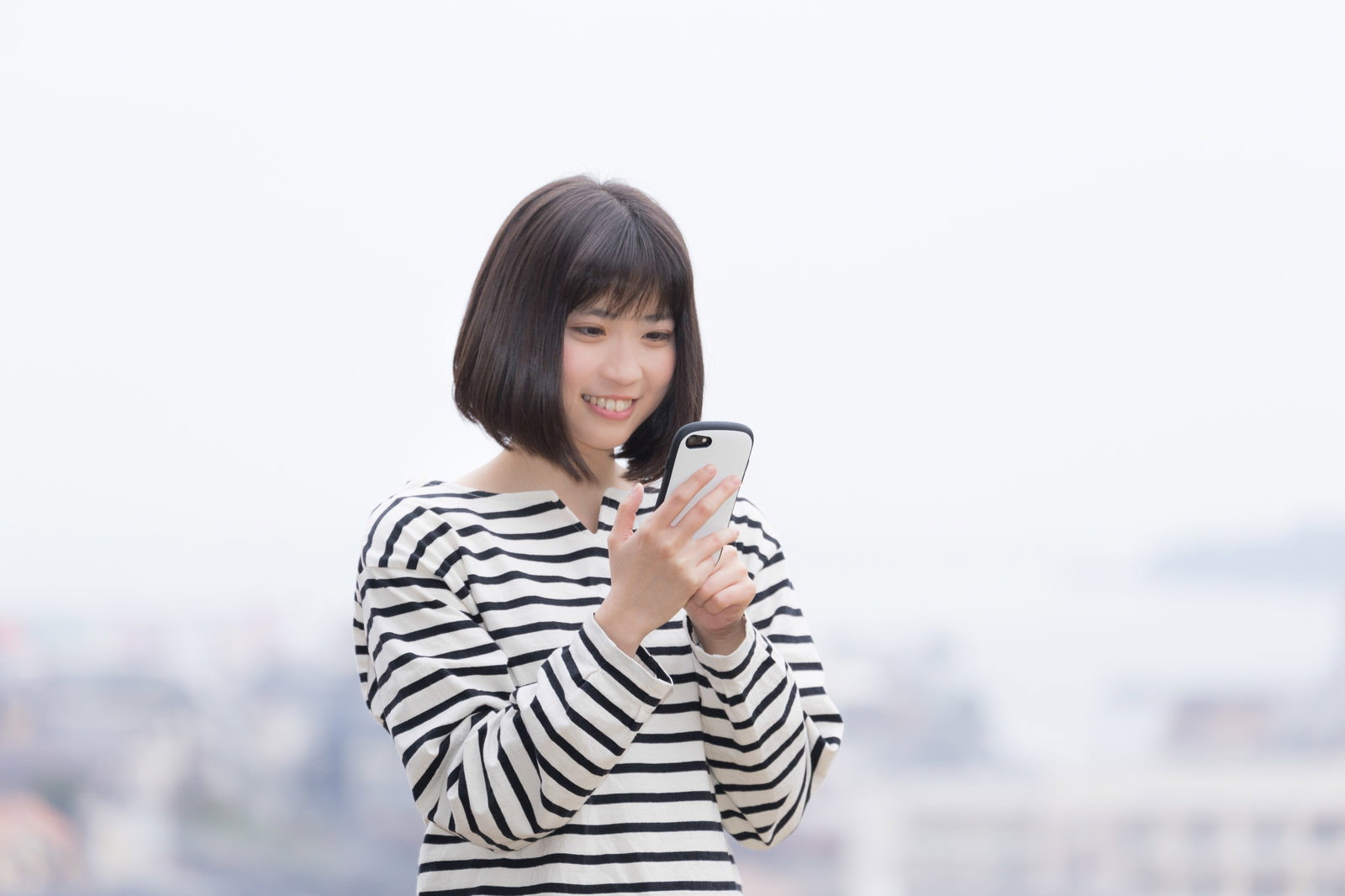 ボーダー柄の服を着た女性がスマートフォンを操作している様子［モデル：塩田みう］