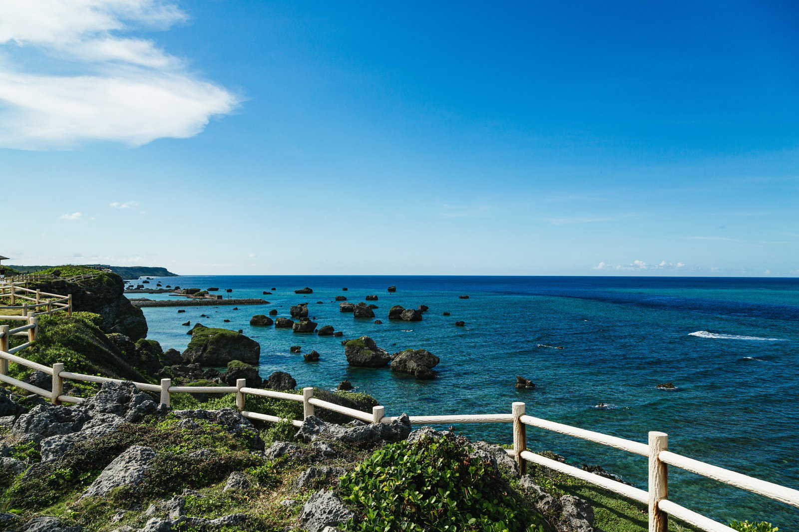 宮古島の海岸で白い柵の先に見える青い海と岩礁