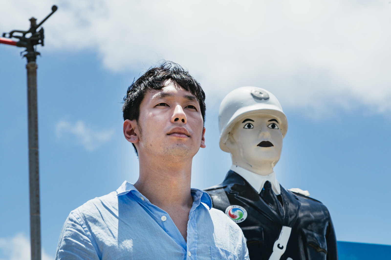 宮古島の宮古まもる君と青空を見上げる青いシャツの男性［モデル：大川竜弥］