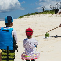 砂浜でスイカ割りのイメトレをする男性と見守る子どもたちの写真