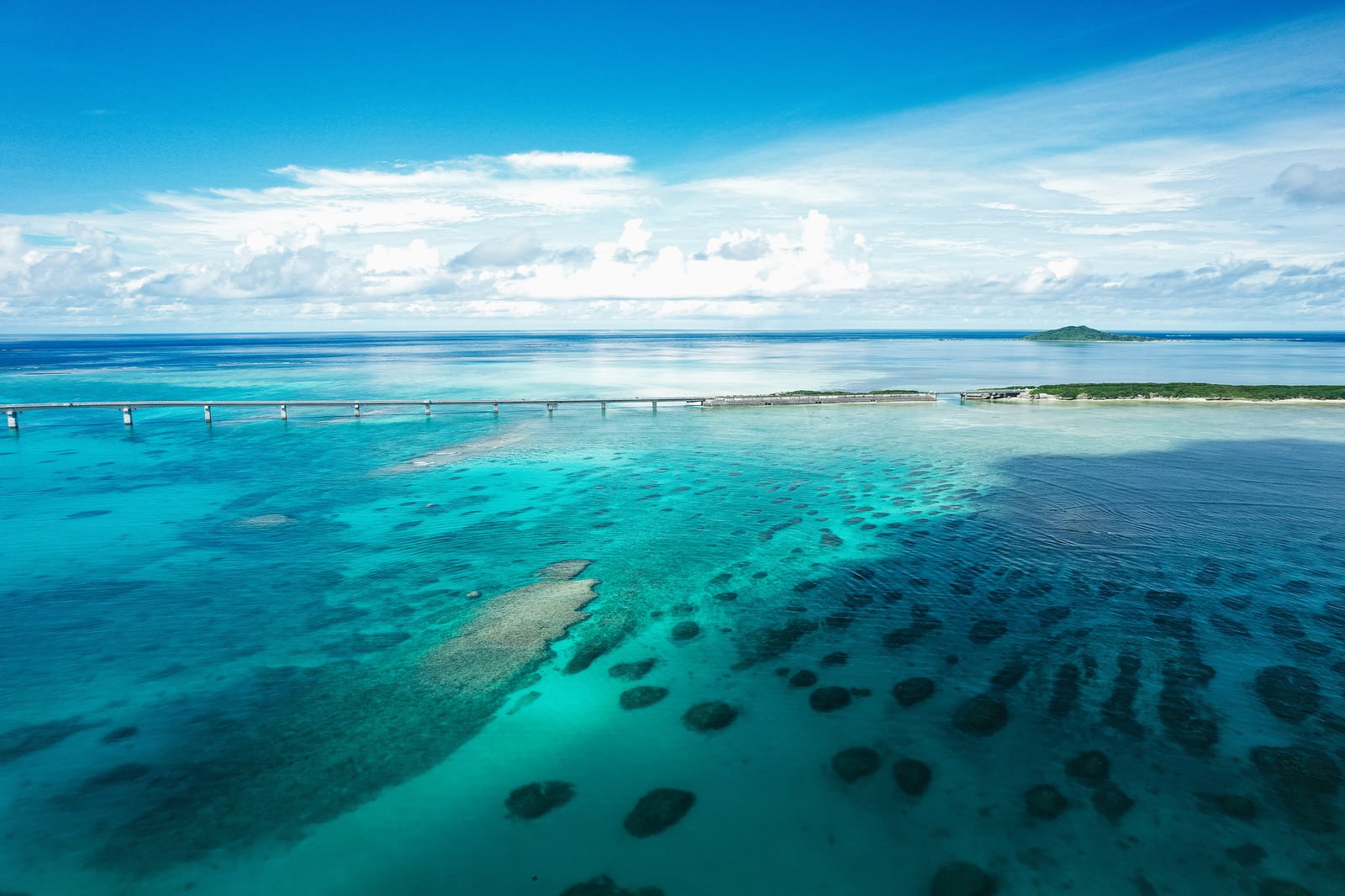 A white Irabu Bridge spanning across the emerald green sea with the seabed visible through the transparent waters