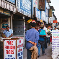食事時に混み合うニューデリーの歩道と屋台の写真