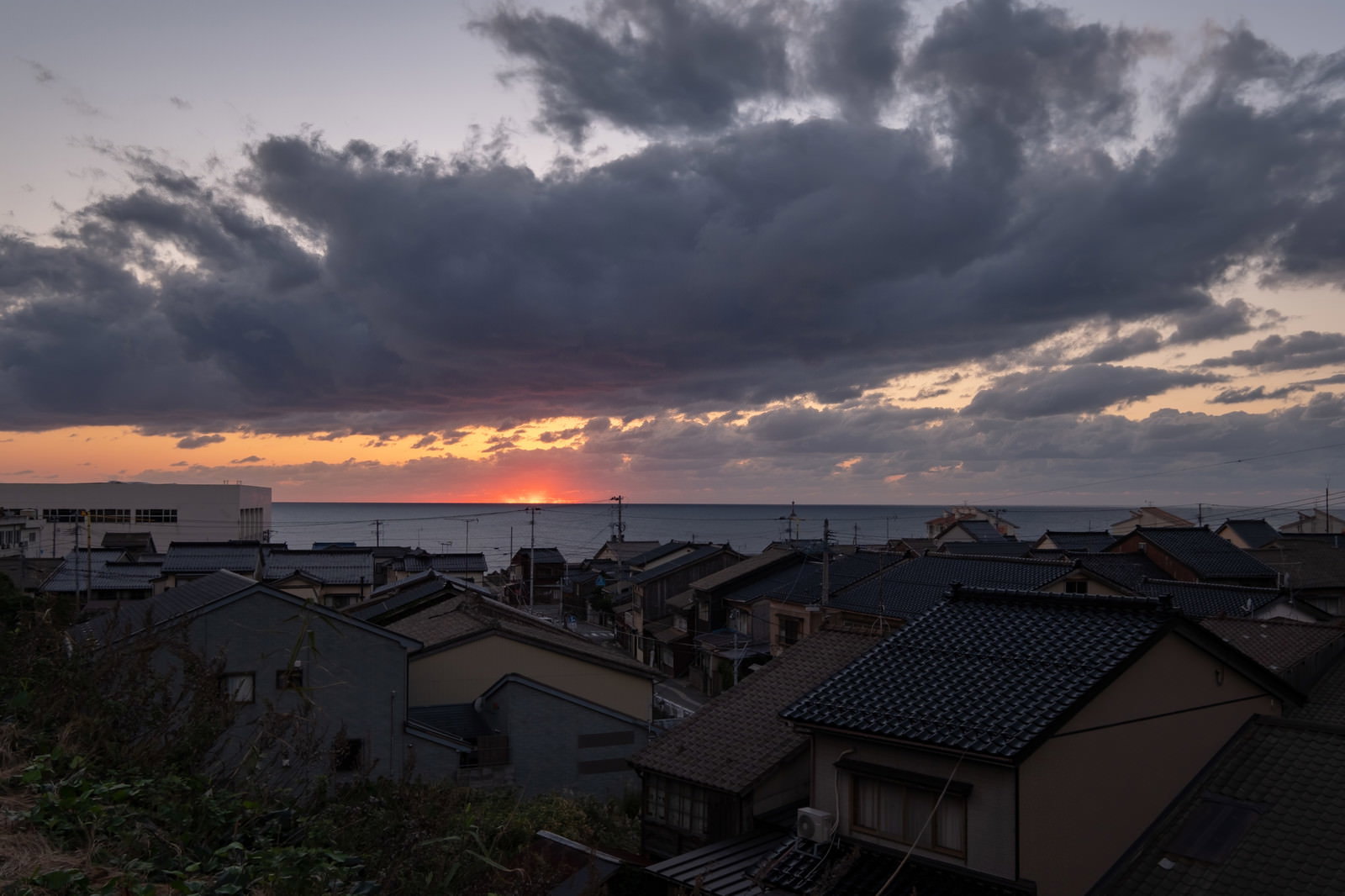 夕焼け空の下、海沿いに立ち並ぶ民家の風景