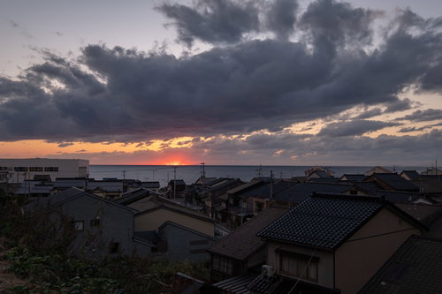 沈む夕日と海沿いの民家の風景 - 夕焼けに染まる住宅街