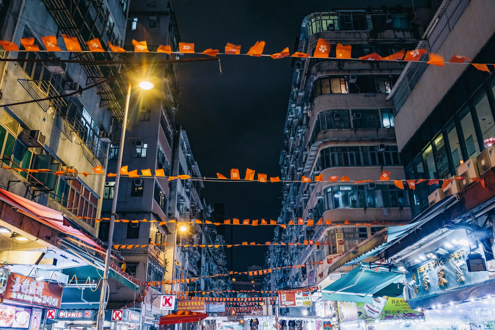 夜の香港の商店街に香港旗が連なって吊るされている風景