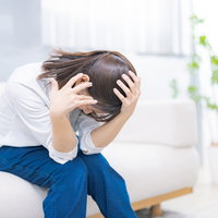 頭が痛くてソファーにうずくまる女性の写真