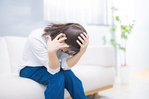 頭が痛くてソファーにうずくまる女性