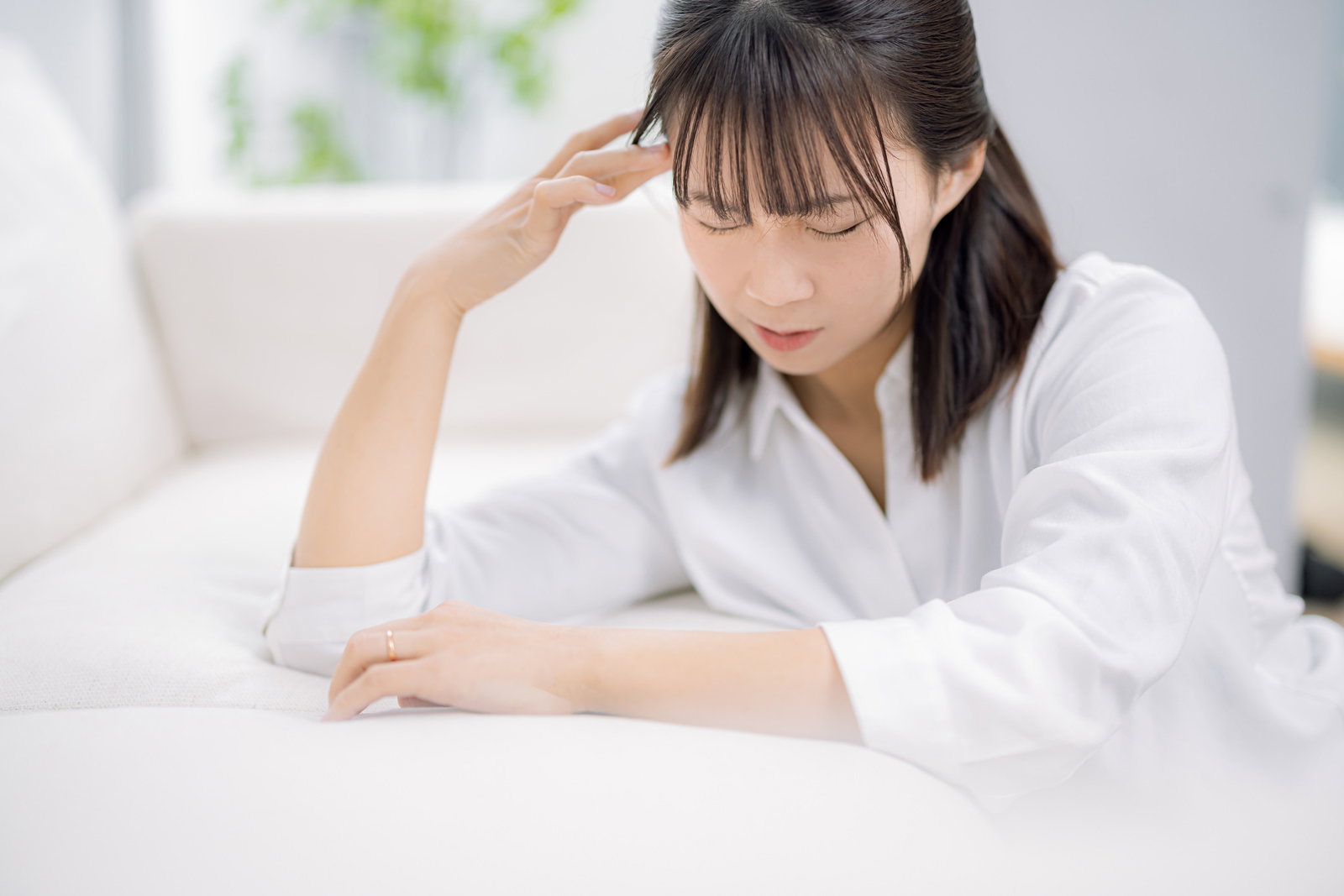 机の前で頭を抱えて目を閉じる、ストレスを感じている女性［モデル：本坊実結］