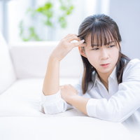 育児ストレスで頭痛に苦しみソファーにもたれかかる女性の写真