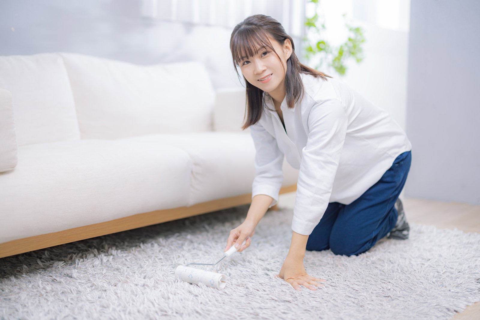 膝をついて絨毯をコロコロクリーナーで掃除する女性［モデル：本坊実結］