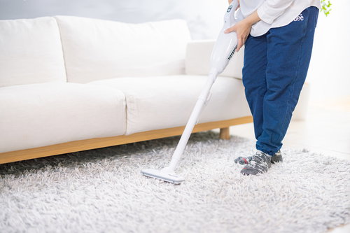 白いソファーの前の絨毯に掃除機をかける女性