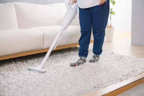 リビングのラグに掃除機をかける男性の様子