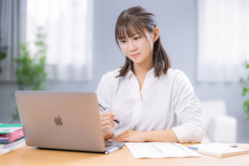 経費をチェックしつつ紙に書く女性