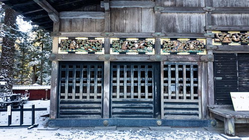 冬の日光東照宮で見る格子戸と上部の三猿の彫刻装飾と雪景色