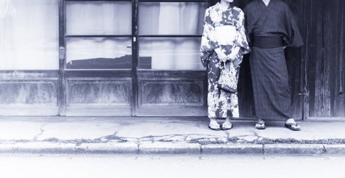 古い建物の前に立つ和装男女のポートレート