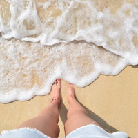 波打ち際に立つ素足と白い波が打ち寄せる砂浜の写真