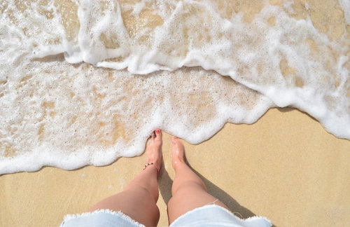 波打ち際に立つ素足と白い波が打ち寄せる砂浜