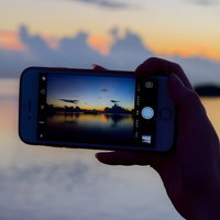 スマホで夕暮れ時の海を撮影する手のシルエットの写真