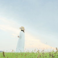麦わら帽子をかぶって草原で遠くを見つめる女性の後ろ姿の写真