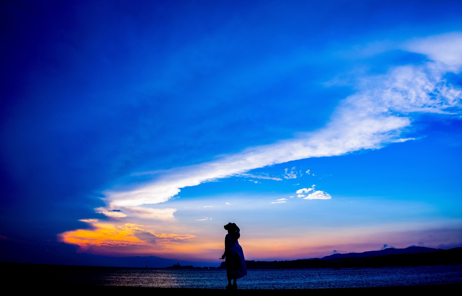 夕焼け空の下、海岸を歩く帽子をかぶった女性のシルエット
