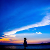トワイライトの海岸を歩く帽子をかぶった女性のシルエットの写真