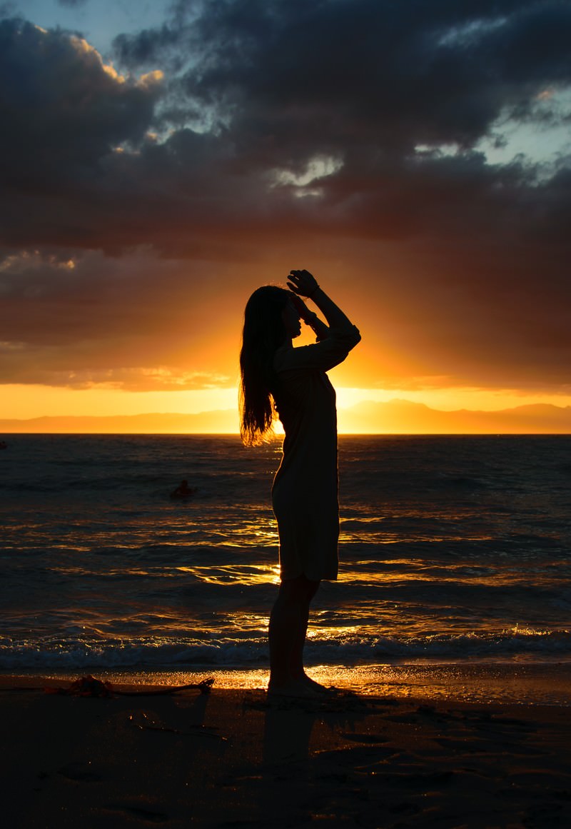 夕焼け空を背景に砂浜で髪をかきあげる女性のシルエット