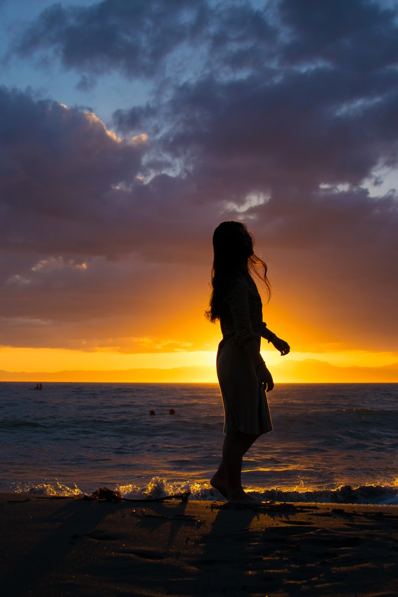 Silhouette of a woman walking on the beach against a sunset sky