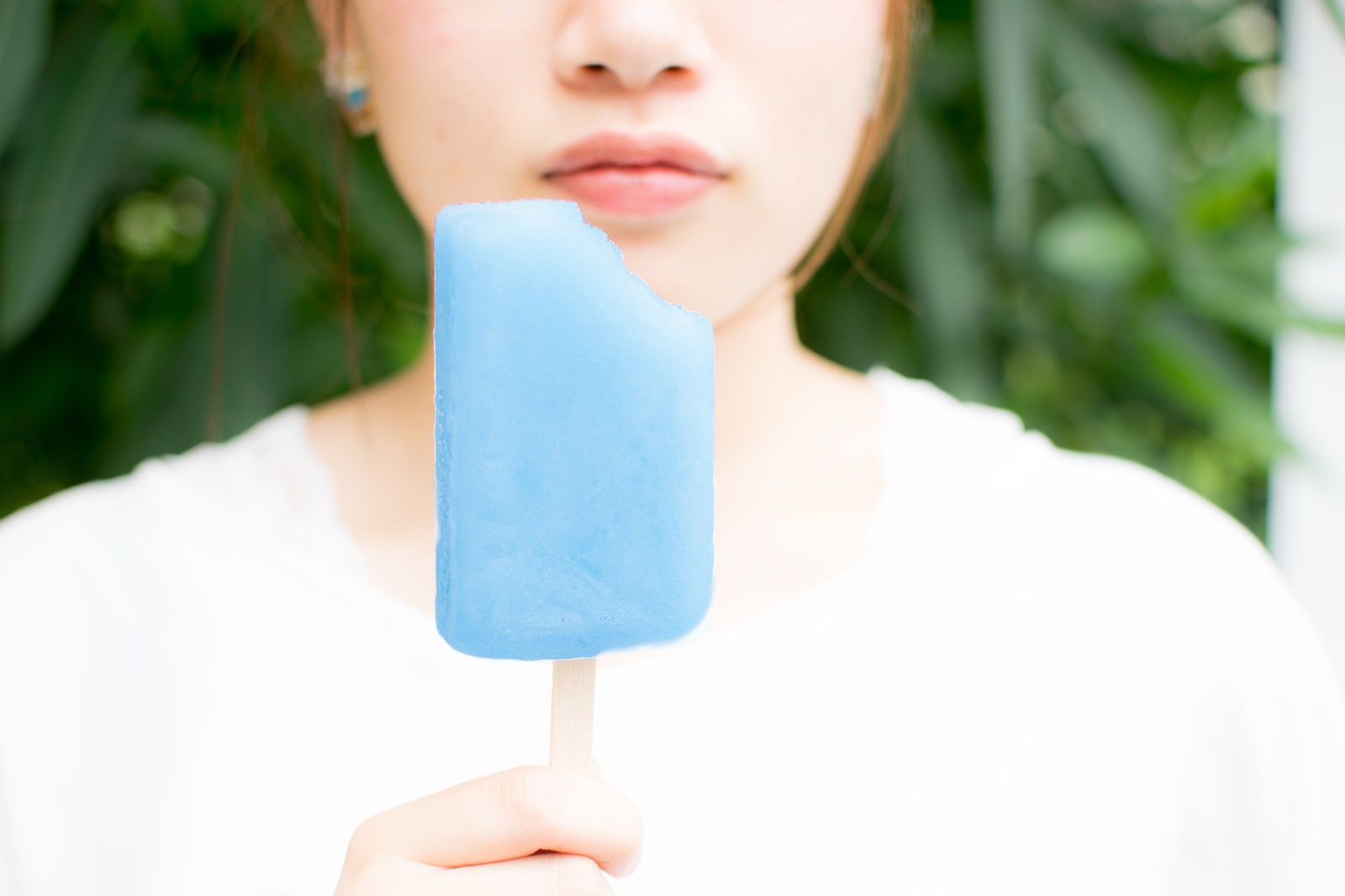 青いソーダ味のアイスバーを手に持って食べる白い服の女性