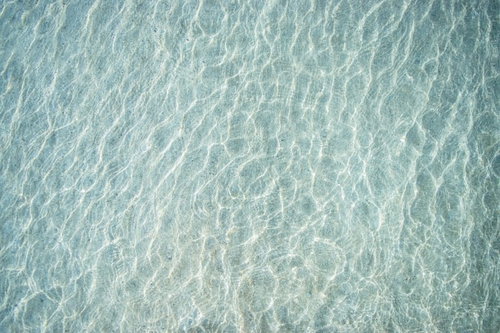 透明な海の浅瀬に砂紋が映るテクスチャ