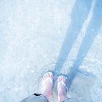 浅瀬で白いビーチサンダルを履いた女性の足元の写真