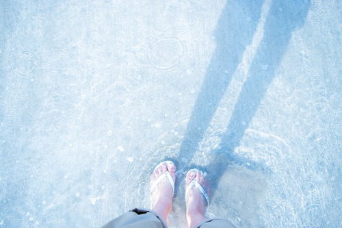 浅瀬で白いビーチサンダルを履いた女性の足元