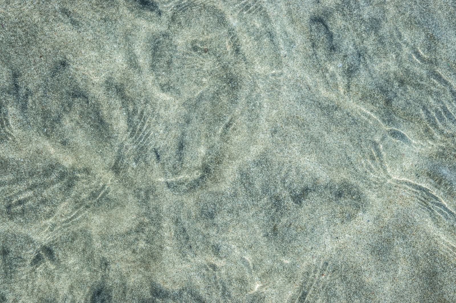海水越しに見える砂地の砂紋模様、波によって作られた自然なテクスチャー