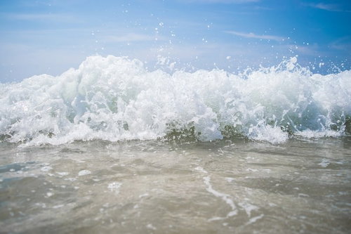 砂浜に打ち寄せる波しぶきが上がる波打ち際
