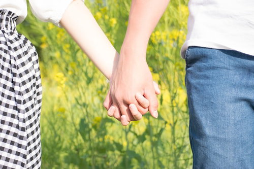 緑の中で恋人つなぎをする男女のカップルの手元
