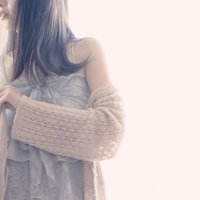 淡いベージュのトッパーカーディガンに袖を通す女性の写真