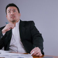 顎に手を当てて斜め上を見上げながら考え込む黒いスーツのビジネスマンの写真