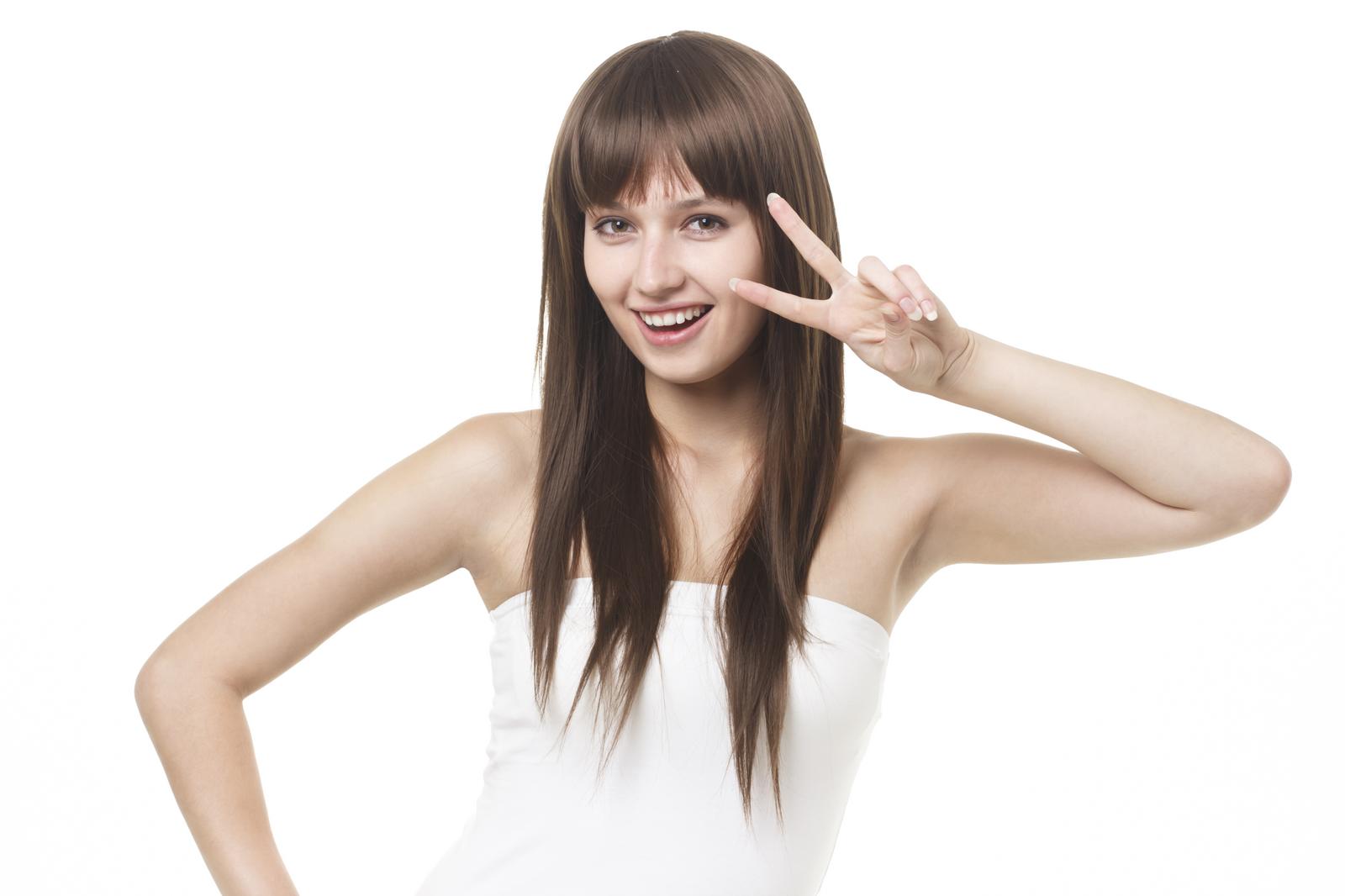 白背景でピースサインをするストレートロングヘアの笑顔の女性［モデル：モデルファクトリー］