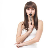 メイクブラシを口元に当てて上を見つめる女性の写真