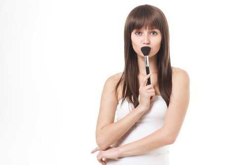 メイクブラシを口元に当てて上を見つめる女性