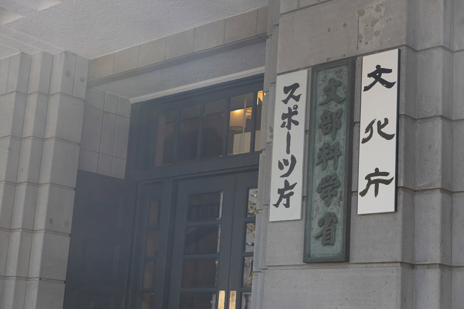 グレーの建物に設置された文部科学省の縦書き銘板と通用口