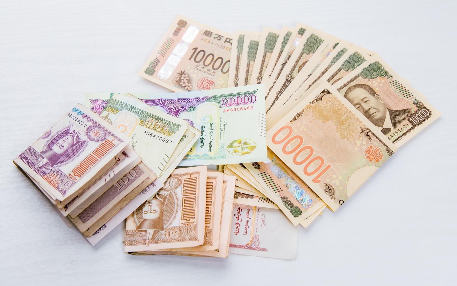 モンゴルのトゥグルグ札と日本の一万円札が白い背景に並べられている